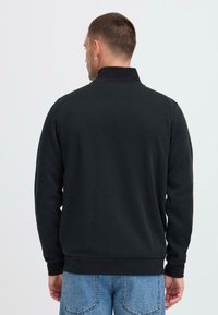 Felpa nera con collo alto, maniche lunghe e orlo a coste. Realizzata in materiale morbido, con una superficie liscia.