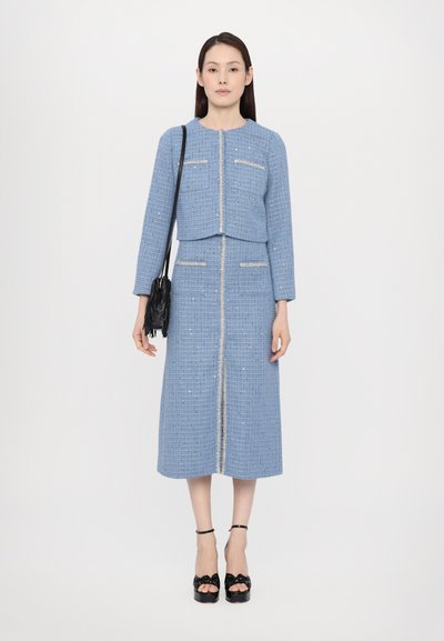 Blaues Tweed-Zweiteiler-Set mit einer cropped Jacke und einem knielangen Rock, ausgestattet mit silberner Stickerei und Taschen, kombiniert mit schwarzen Plateausandalen.