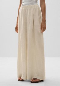 Light beige wide-leg trousers with vertical stripes, elastic waistband, and side pockets, made from a textured fabric. Pair with flat sandals.