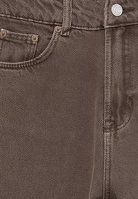 Ruskeat farkut, joissa on klassinen viiden taskun muotoilu, hienovarainen pinta, metallinappi ja kontrastiväriset ompelutiedot.