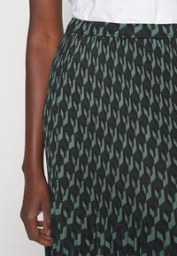 Záhybová sukně v černé a zelené barvě s geometrickým vzorem. Vyznačuje se texturovanou tkaninou a elastickým pasem pro pohodlí.