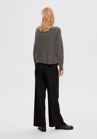 Harmaa teksturoitu neule, jolla on lyhennetty malli, päällä mustat leveälahkeiset housut. Yksinkertainen pääntie ja pitkät hihat.