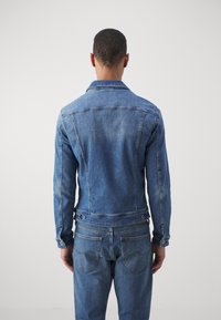 Jeansjacka i ljusblått med klassisk krage, knappade manschetter och en figursydd design. Har en lätt blekning och två bakfickor.