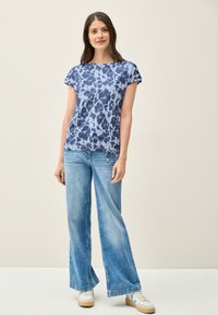 Top azul de manga corta con un patrón floral, combinado con jeans de pierna ancha de color azul claro y zapatillas blancas. Tejido suave con un corte relajado.