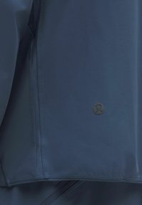 Marineblauwe sportjack met een gladde textuur, een mesh ventilatiepaneel en een klein zwart logo aan de zoom.