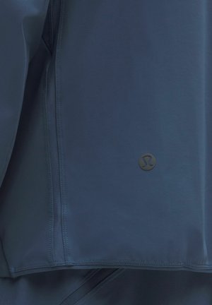 Marineblaue Sportjacke mit glatter Textur, Netzbelüftungsbereich und kleinem schwarzen Logo am Saum.