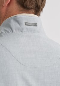 Hellgraues Hemd mit weicher Textur und hohem Kragen, der eine genähte Detailierung sowie ein rechteckiges Markenschild auf der Rückseite aufweist.