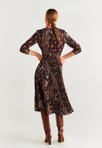 Robe noire à motif floral avec manches trois-quarts, jupe plissée, tissu à motifs, et bottes marron montant aux genoux. Le design présente des accents rouges et dorés vibrants.
