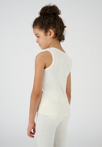 Top senza maniche di colore crema chiaro in morbido cotone, con scollatura rotonda, abbinato a leggings di colore chiaro.