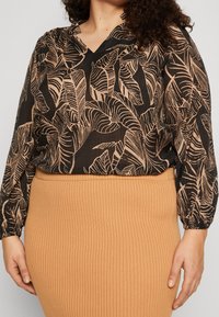 Svart blus med beige lövmönster, V-ringning och långärmar, tillsammans med en ribbad, knä-lång, kamelfärgad kjol.