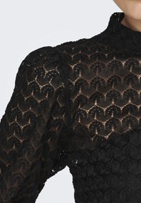 Sort blonde bluse med indviklede blomster mønstre, høj krave og puff ærmer, med en semi-gennemsigtig, struktureret overflade.