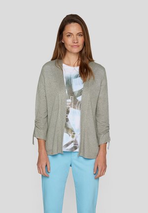 Hellgrauer Cardigan mit schimmernder Textur, offene Vorderseite, Dreiviertelärmel, über einem grafisch bedruckten Shirt und hellblauen Hosen getragen.