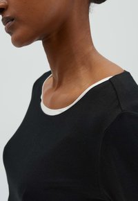 Chemise en coton noir mettant en avant un col en scoop souligné de blanc, d'une texture lisse et d'un design ajusté, mettant en valeur la zone des épaules et du cou.
