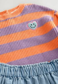 Pasiasty sweter w pomarańczowo-fioletowym prążkowanym materiale z naszywką w kształcie serca i uśmiechem. Na dole miękki, niebieski zbierany materiał.