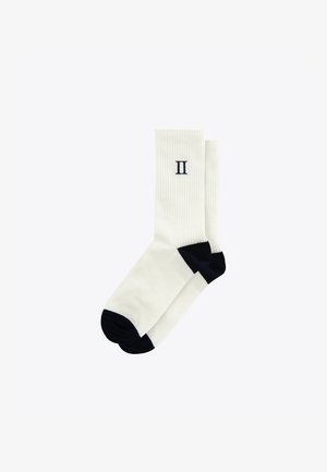 White ribbed socks with navy blue toe and heel accents. Features a stitched numeral "II" on the side, made from a soft, flexible fabric.