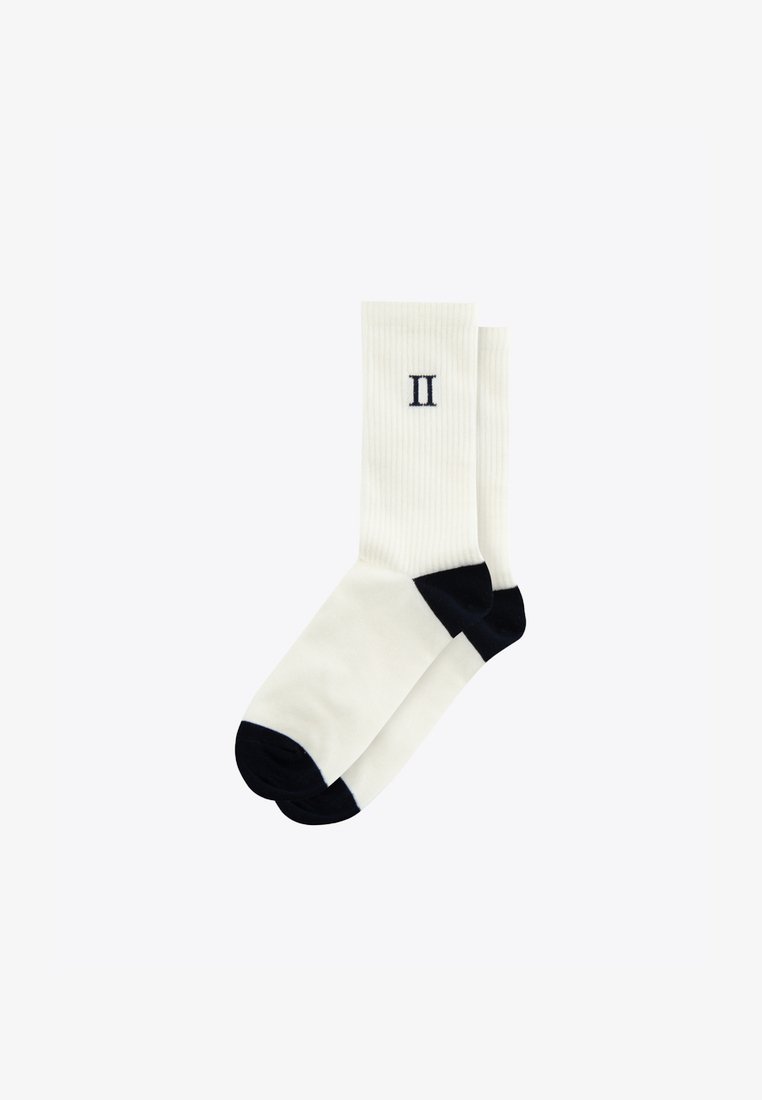 Meias brancas caneladas com acentos em azul-marinho no bico e no calcanhar. Apresenta um numeral "II" bordado na lateral, feito de um tecido suave e flexível.