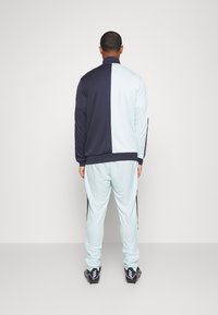 Trainingsanzug mit einem geteilten Design: dunkelblau und hellblau. Hergestellt aus glattem Stoff mit kontrastierenden schwarzen Seitenakzenten und gerippten Bündchen.