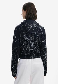 Sudadera negra con un patrón de telaraña geométrica en tonos plateados, que presenta una capucha con cordones y puños y dobladillo acanalados.