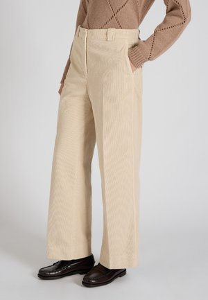 Pantalons larges en velours côtelé beige avec une finition texturée, dotés de poches latérales et d'une ceinture standard, associés à des mocassins marron foncé.