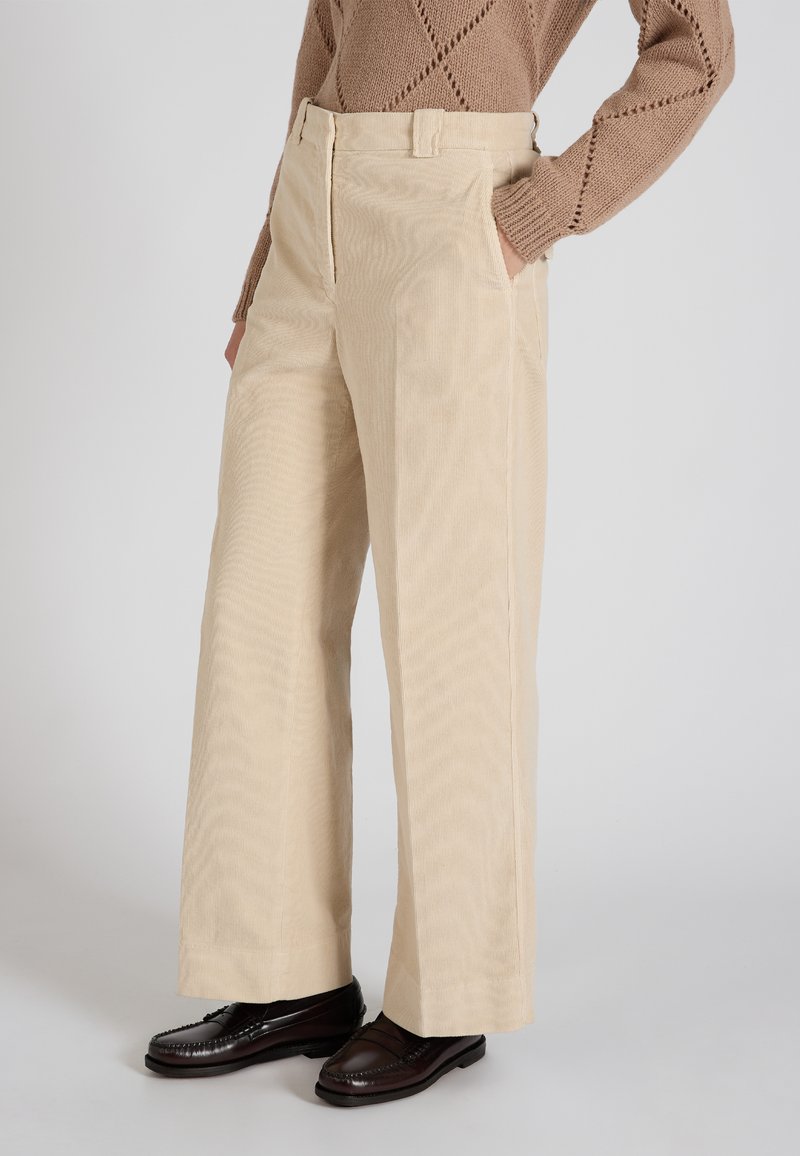 Beige corduroy wijde-broek met een textuurafwerking, voorzien van zijzakken en een standaard tailleband, gecombineerd met donkergroene instappers.