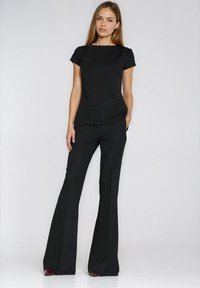 Czarny top z krótkim rękawem o teksturowanej tkaninie i okrągłym dekolcie, zestawiony z czarnymi rozszerzanymi spodniami. Strój cechuje prosty design.
