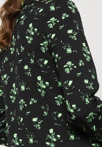 Czarna koszula z długim rękawem, zdobiona żywym zielonym wzorem kwiatowym, o gładkiej fakturze i dopasowanym kroju, widocznym w okolicy ramion.
