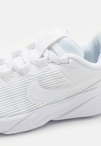 Vitaid sportskor med ett strukturerat, randigt ovandel, mjukt tygfoder och en framträdande vit Nike-swoosh-logotyp på sidan.