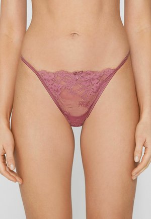 Žena nosící bikiny z mávelové krajky s květinovým vzorem a malou mašlí uprostřed přední části, zobrazená od pasu po střed stehen.