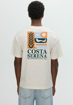Persona con cabello corto y rizado lleva una camiseta beige con gráfico colorido y texto "Costa Serena Mediterranean Spirit 2005" en la parte trasera.