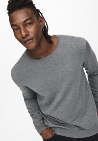 Grijze lange mouwen trui met een ronde halslijn, gladde textuur en aansluitende mouwen, gecombineerd met donkere denim jeans. Eenvoudig en casual ontwerp.