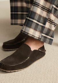 Brune ruskind slip-on sko med en scalloped design og kontraststing, parret med ternede bukser i beige, marineblå og brune nuancer.