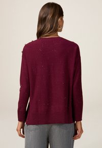 Pull bordeaux à manches longues, avec une coupe légèrement ample et de subtils paillettes répartis sur toute la surface. Ourlet côtelé et détail de design au dos.