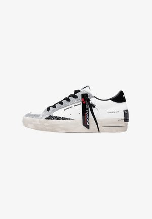 Sneaker bianca low-top con lacci neri, dettagli glitter argento, linguetta nera sul tallone e un'etichetta nera con la scritta "CRIME LONDON" attaccata ai lacci.