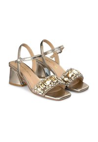 Metallisch goldene Blockabsatzsandalen mit einem breiten, verzierten Oberteil, das mit klaren und goldenen Steinen besetzt ist. Verstellbarer Knöchelriemen für die perfekte Passform.