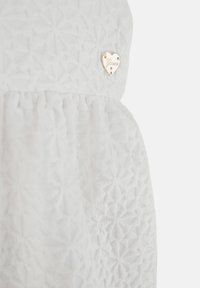 Vestido blanco con tejido texturizado de patrón en diamante. Presenta un acento de logo en forma de corazón dorado cerca de la cintura.