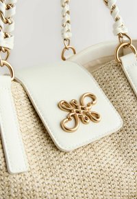 Sac à main en cuir blanc avec une base en paille tressée, équipé d'une fermeture décorative en métal doré et d'une bandoulière tressée.