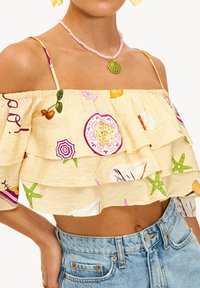 Haut court jaune épaules dénudées avec des volants superposés, présentant des motifs colorés de fruits et d'étoiles de mer, associé à un short en denim taille haute.