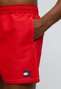 Κόκκινα μαγιό βερμούδα από απαλό ύφασμα με ελαστική μέση, πλευρική τσέπη και μπλε σκούρο ταμπελάκι με το λογότυπο "TOMMY JEANS".