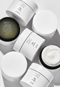 Cinque barattoli cosmetici, bianchi con testo nero. Due barattoli contengono un gel trasparente e una crema. Forma arrotondata con finiture lisce.