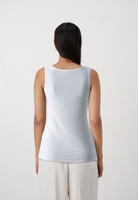 Top sin mangas blanco ajustado con textura acanalada y escote redondeado, visto desde la parte posterior. Tejido suave sin adornos visibles.