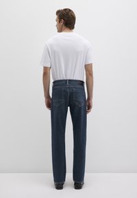 Dark blue denim jeans with a loose fit, five-pocket design, and a black waistband label. Worn with a plain white t-shirt.