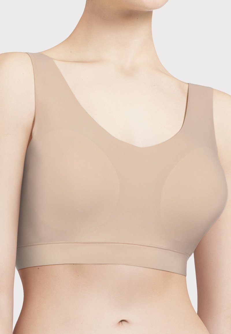Beige sømløs bh med brede stropper, lav V-hals og en jevn, elastisk tekstur. Har subtil formgivning for komfort og støtte.