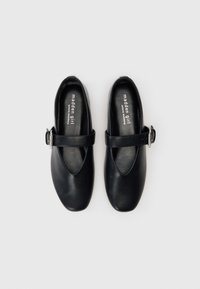 Sapatos de couro pretos com um bico oval, uma tira com uma fivela prateada na parte média do pé e uma textura suave.