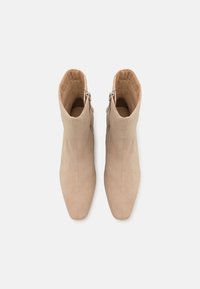 Béžové semišové kotníkové boty s špičatou špičkou, bočním zipem a hladkým povrchem. Minimalistický design bez dalších vzorů nebo akcentů.