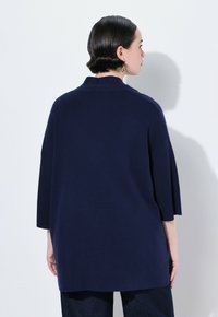 Tyrkysový pletený oversized top s vysokým límcem a širokými rukávy, který se vyznačuje hladkou strukturou a minimalistickým designem.
