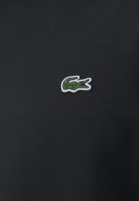 Polo shirt en coton noir avec un petit logo de crocodile brodé en vert avec des détails rouges sur le côté gauche de la poitrine.