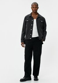 Zwarte spijkerjack met twee borstzakken, zilveren hardware en contrasterende stiksels. Gedragen over een witte tanktop en gecombineerd met zwarte broek.