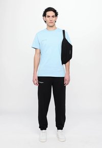 Lyseblå bomulds T-shirt med korte ærmer, sorte sweatpants og en sort skuldertaske. Hvide sneakers afslutter outfittet.