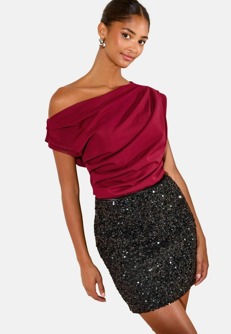 Burgundijas off-the-shoulder tops ar drapēta dizainu, apvienots ar melnu spīdīgu mini svārku. Gluda auduma, spīdīga tekstūra un pieguļošs siluets.