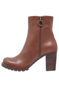 Bottine en cuir marron avec un bout rond, fermeture éclair sur le côté avec une tirette circulaire, et un talon empilé texturé.